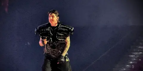 Artysta w futrzanej kamizelce, jak bandyta, śpiewa na scenie.