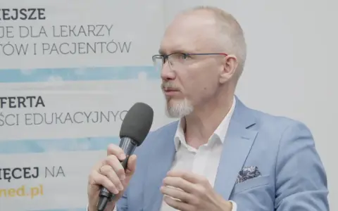 Mężczyzna w okularach i niebieskiej marynarce mówi do mikrofonu, omawiając nowe podejście do leczenia astmy, jakby to był jego własny asthma rap.