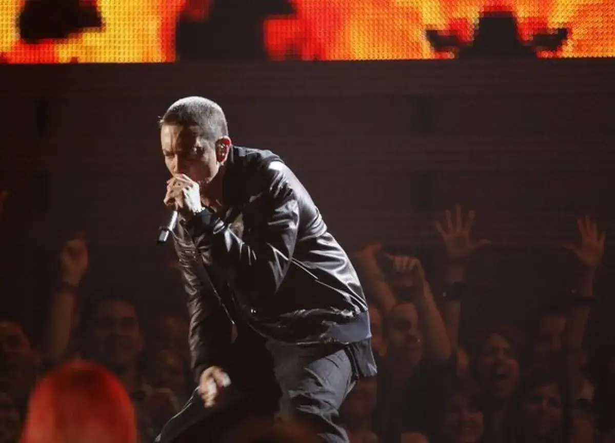 Eminem, znany z tego, jak ma na imię, występuje na scenie w skórzanej kurtce, śpiewając do mikrofonu. Tłum wiwatuje.