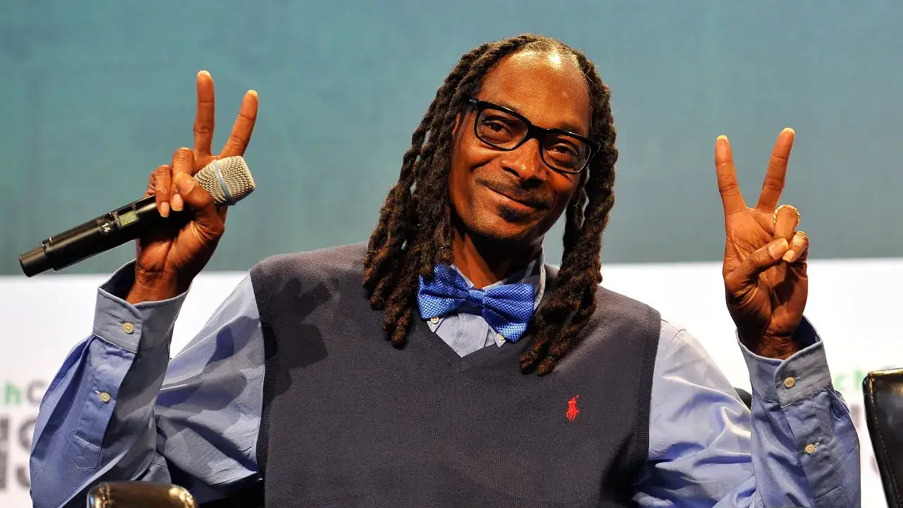 Snoop Dogg z mikrofonem i dwoma palcami w górze, jakby pytał