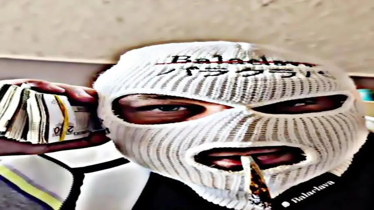 Osoba w masce balaclava trzyma plik banknotów. Widać jej oczy i usta, przez które przechodzi papieros.